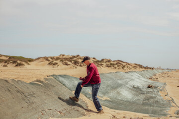 Naklejka premium A man climbs a sand dune covered with a net to catch fuel oil from the sea, on a beach on a sunny day