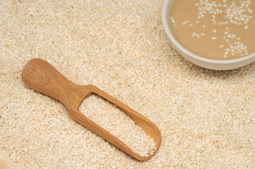 Board with sesame seeds and bowl of tasty tahini on travertine table, closeup