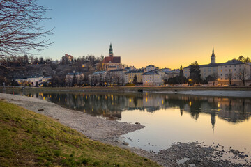 Cityscape of Salzburg, Austria at sunset with the church Maria Himmelfahrt and the Mönchsberg hill reflected in the Salzach river
