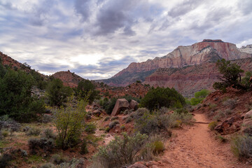 Red rock canyon trail with dramatic clouds and mountains.