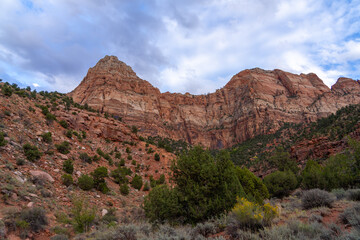 Red rock mountains under a cloudy sky with desert vegetation.