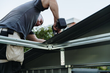 Mature worker installing roofing sheets with drill on metal shed. © Nataliya