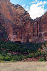 Waterfall cascades down a massive red rock cliff face.