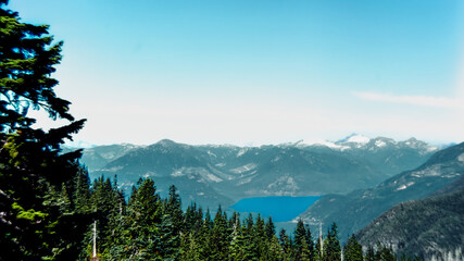 Rocky Mountains surrounding a small lake under a blue wispy sky framed by pine trees in the foregorund.