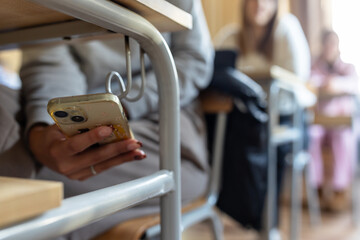 Student using smartphone discreetly in classroom under desk