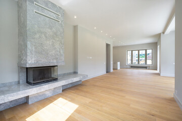 Spacious living room features a sleek stone fireplace, hardwood flooring, and large windows that let in abundant natural light, creating a welcoming atmosphere.
