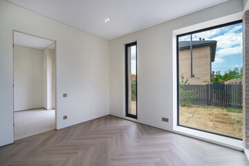 Spacious empty room featuring large windows that allow natural light to fill the space. The view includes a grassy area and wooden fence outside in a peaceful suburb.