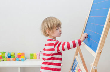 Cute little child drawing with chalk on a blackboard at home, creative and funny indoor activity for children
