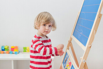 Cute little child drawing with chalk on a blackboard at home, creative and funny indoor activity for children
