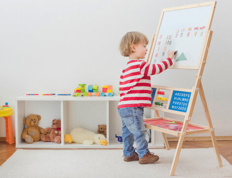 Cute little child playing at a magnetic board, learning letters, numbers and geometric shapes at home. Educative and funny indoor activity for early development. - Powered by Adobe