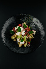 Fresh summer salad with tomato, cucumber, feta cheese, red onion and mint leaves served in a black bowl. Healthy vegetarian meal, gourmet restaurant food concept.
