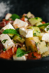 Fresh summer salad with tomato, cucumber, feta cheese, red onion and mint leaves served in a black bowl. Healthy vegetarian meal, gourmet restaurant food concept.
