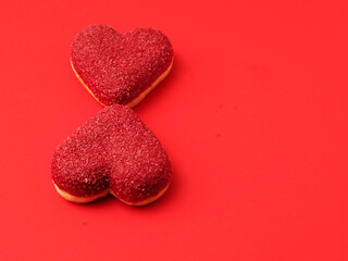 Obraz premium Two heart shaped doughnuts on red color surface. Top of the product is covered with colored sweet icing. Food for a Valentine day or special romantic event. Creative bakery product.
