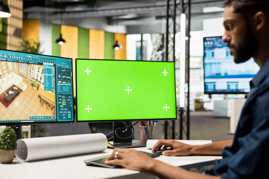 Middle eastern contractor prepares apartment floor plan next to copy space monitor, decorating and designing the new construction building layout. 3D software for interior design.