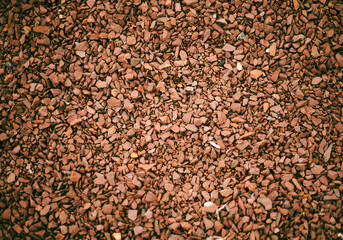 A detailed close-up of small red gravel rocks spread across the ground. The uneven texture and various sizes create an interesting visual pattern.