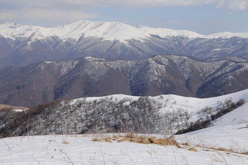Snowy slope with emerging dry grass and layered mountain ridges, Lori, Armenia