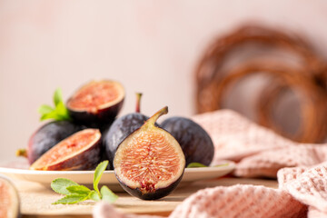 Sliced fig halves and whole figs arranged on a plate with fresh stevia leaves A rustic scene with a woven basket and pink napkin in soft light