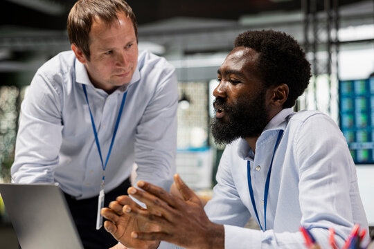 Diverse male coworkers planning business projects at desk. Caucasian and african american men using digital device for corporate growth, strategy, teamwork and productivity in modern office.