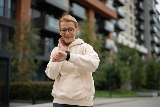 Mature woman checking pulse on smartwatch in urban setting