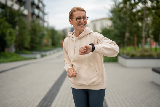 Happy senior woman tracking fitness on smartwatch outdoors