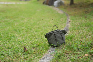 A green purse is laying on the grass next to a stone path