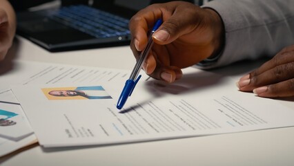 Close up of CV document evaluation in a corporate job interview, businesswoman asking african american candidate questions based on his past work experience and studies shown on paper. Camera B.