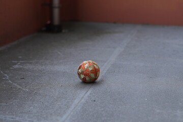 A small orange and green ball is sitting on a grey concrete floor