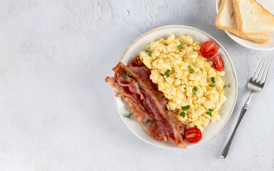 Scrambled eggs with crispy bacon and tomatoes on a white background. Top view. Copy space. 
