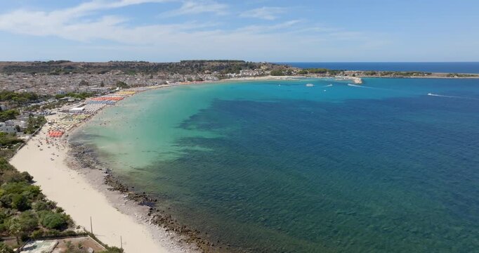 Aerial view of the beach of San Vito Lo Capo, a tourist destination in the province of Trapani, Sicily, Italy. There are many beach umbrellas and tourists at the beach resorts along the coast.