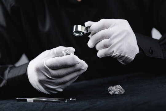 Jeweler examining rough and polished diamonds with loupe, black background