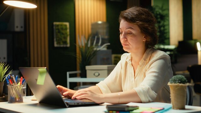 Fototapeta Tensed businesswoman stretching her upper back and neck muscles, correcting her chair posture and neck stiffness due to intense office activity. Discomfort and weariness. Camera B.
