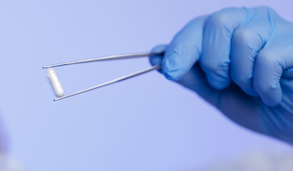 Gloved hand holding capsule with tweezers on blue background