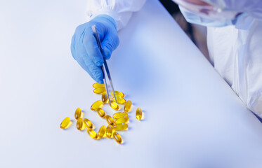 Scientist in lab coat analyzing yellow gel capsules with tweezers