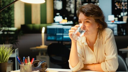 Worker building a presentation with organized agenda while drinking water, enterprise annual report. After hours, woman committed to scheduling, researching and documenting strategies. Camera B.