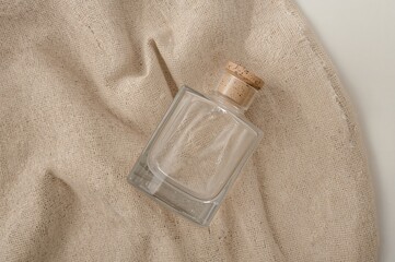 Still life of a clear glass bottle with a cork stopper lying on a textured beige fabric surface