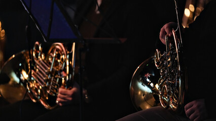 Fototapeta premium Close up of orchestra brass section featuring french horn and trumpet with golden reflections and bokeh lights in dark moody background