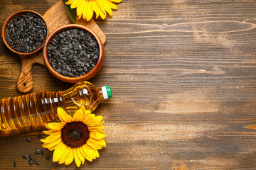 Bottle of oil, sunflowers and bowls with seeds on wooden background