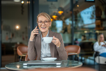 Mature businesswoman smiling while talking on phone at urban cafe