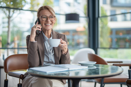 Mature businesswoman talking on smartphone drinking coffee - Powered by Adobe
