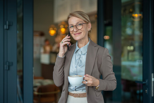Mature businesswoman talking on phone holding coffee cup - Powered by Adobe