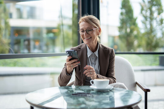 Mature businesswoman smiling while using smartphone at cafe