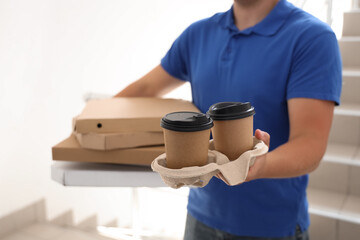 Male courier with pizza boxes and coffee cups in stairway, closeup