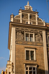 A grand historic facade featuring intricate tile mosaics, brickwork, and sculpted details under a clear blue sky. The ornate architecture 