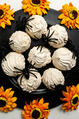 Halloween Food Flat Lay: Skeleton Hands Grabbing Spooky Meringue Cookies with Spiders and Sunflowers on Black Tray