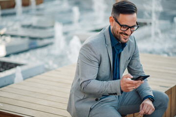 Fototapeta premium Smiling businessman using smartphone near fountain in city