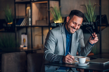 Happy businessman taking notes and smiling in a cafe