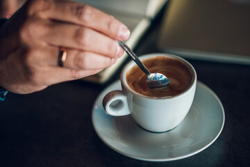 Close up of man stirring coffee in cafe with book and laptop