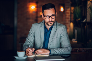 Businessman writing notes in notebook at cafe