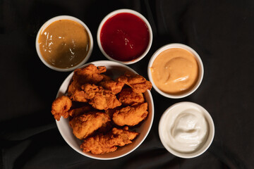 Top view of a bowl of fried chicken with sauces on top of a black cloth.