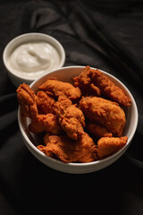 Top view of a bowl of fried chicken with mayonnaise on top of a black cloth.